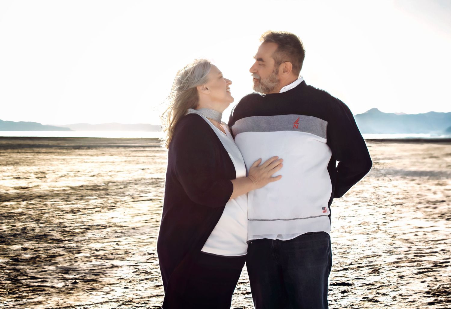 Couple sharing intimate moment on beach at sunset with mountains in background.