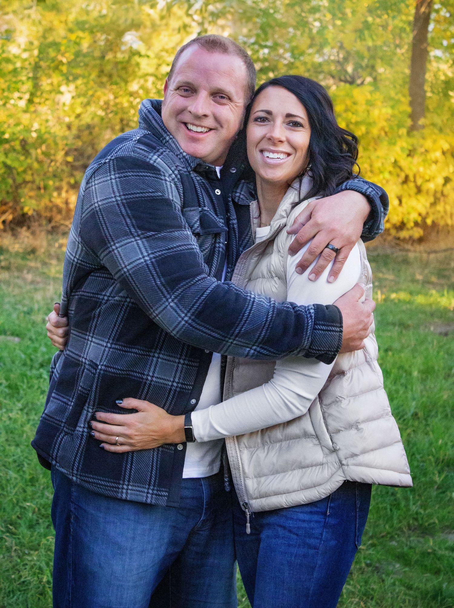 A couple shares playful moments outdoors in plaid and puffy vest during golden hour.