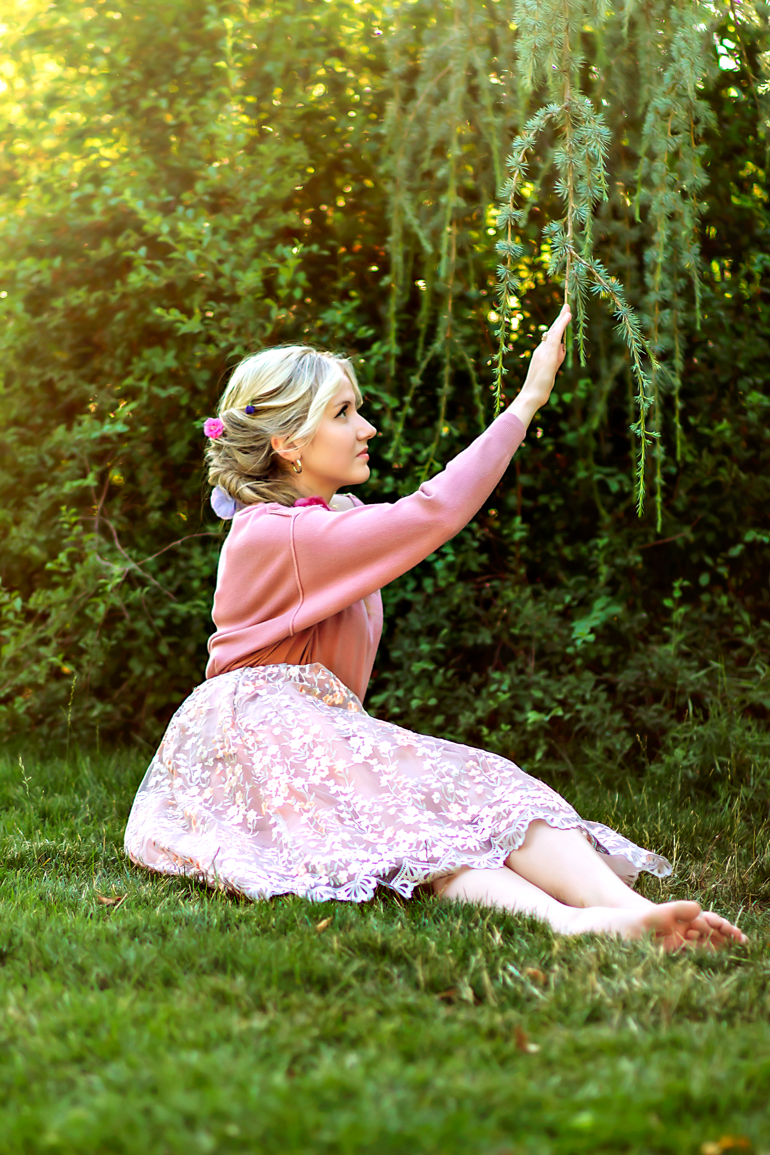 A person in a pink floral dress lies gracefully on green grass during a summer photoshoot.