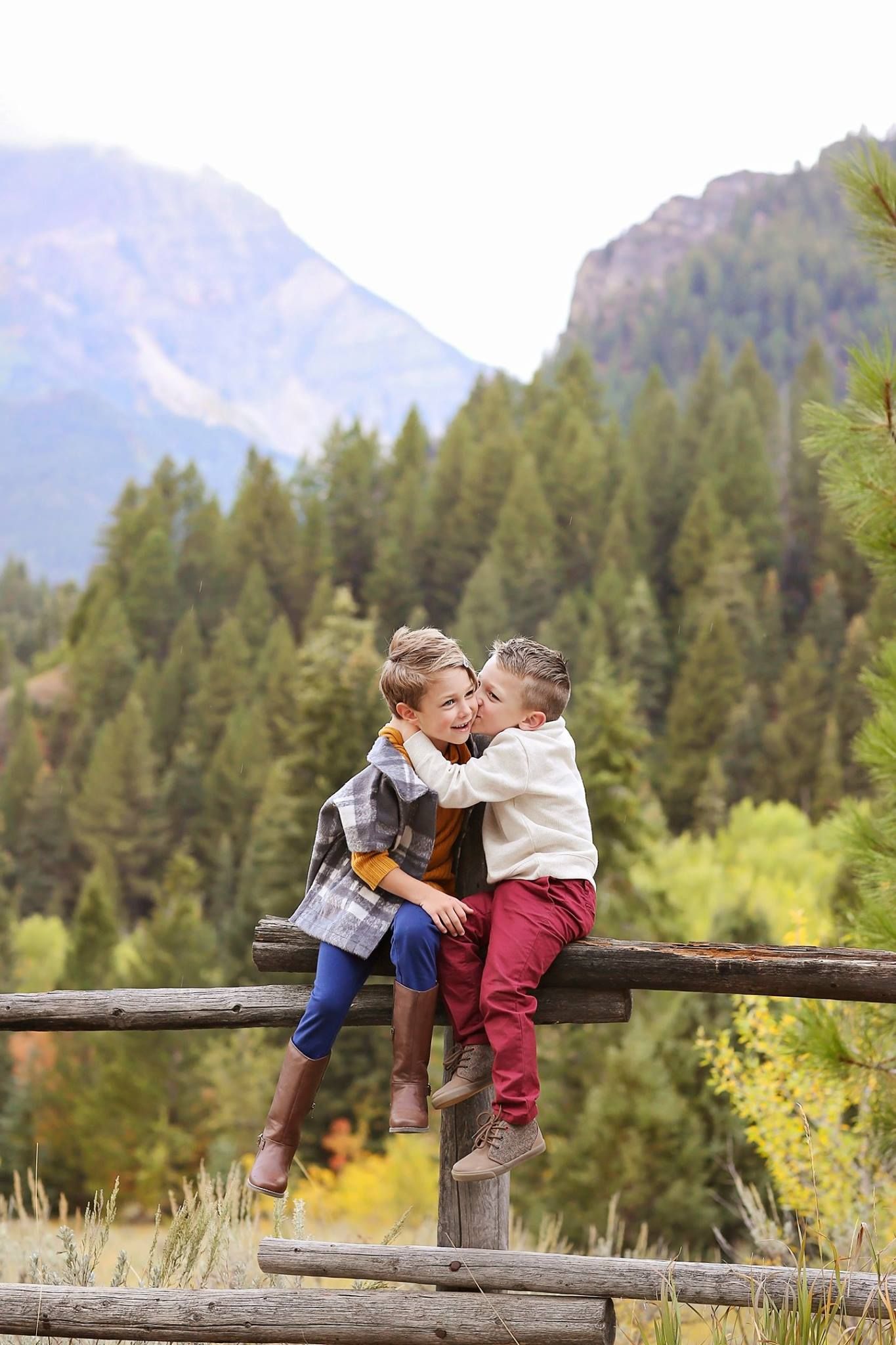 Children sitting on wooden fence with mountain landscape in background.