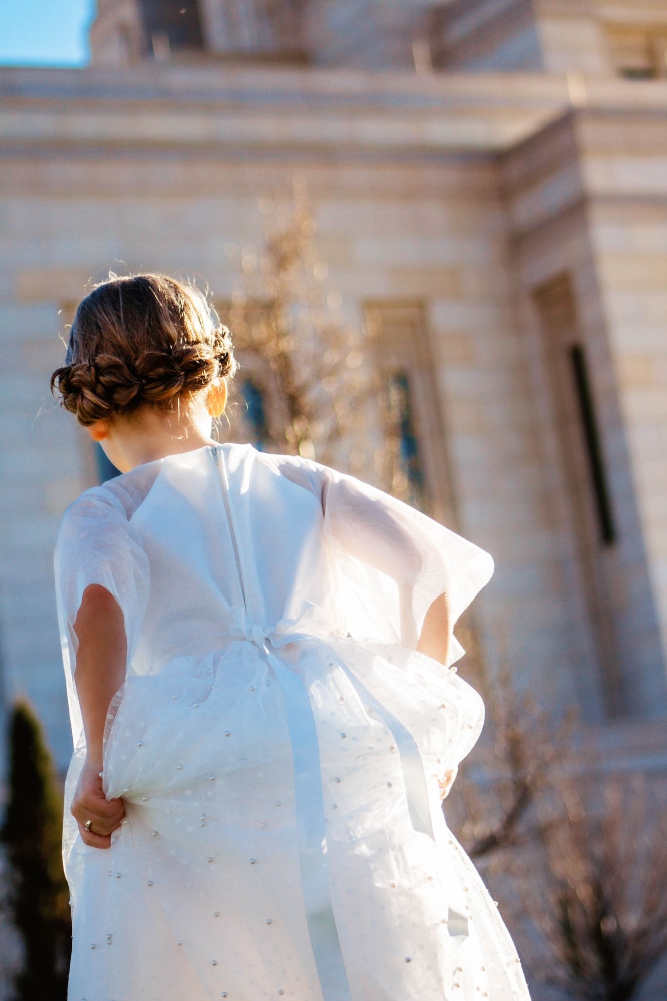 Back view of a white dress with flowing fabric against an architectural backdrop.