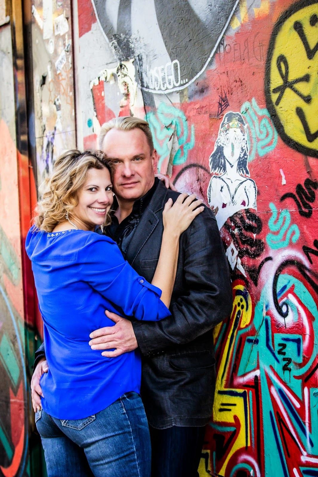 Couple posing against colorful graffiti wall in urban setting.