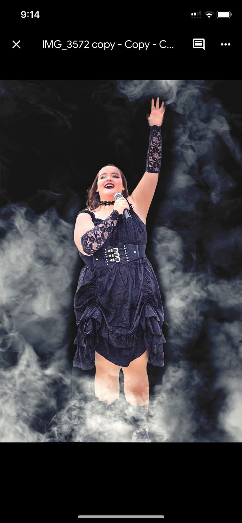 Performer in gothic dress strikes dynamic pose surrounded by atmospheric gray smoke.