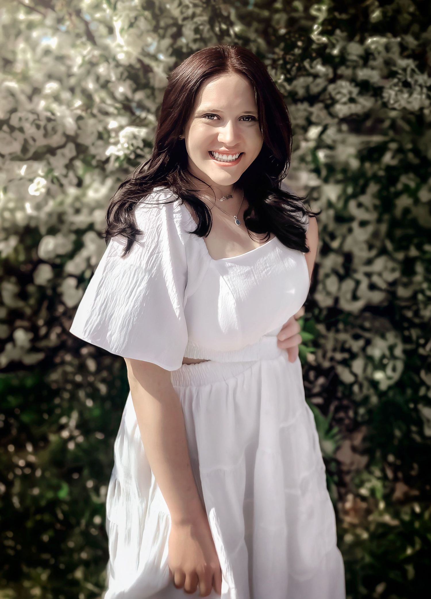 Person in white dress smiling against blooming spring foliage background.