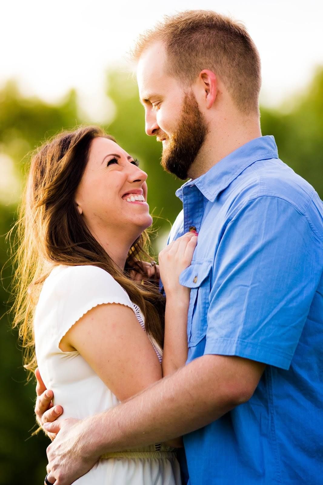 Romantic couple embraces outdoors in a sunlit garden setting during a photoshoot.