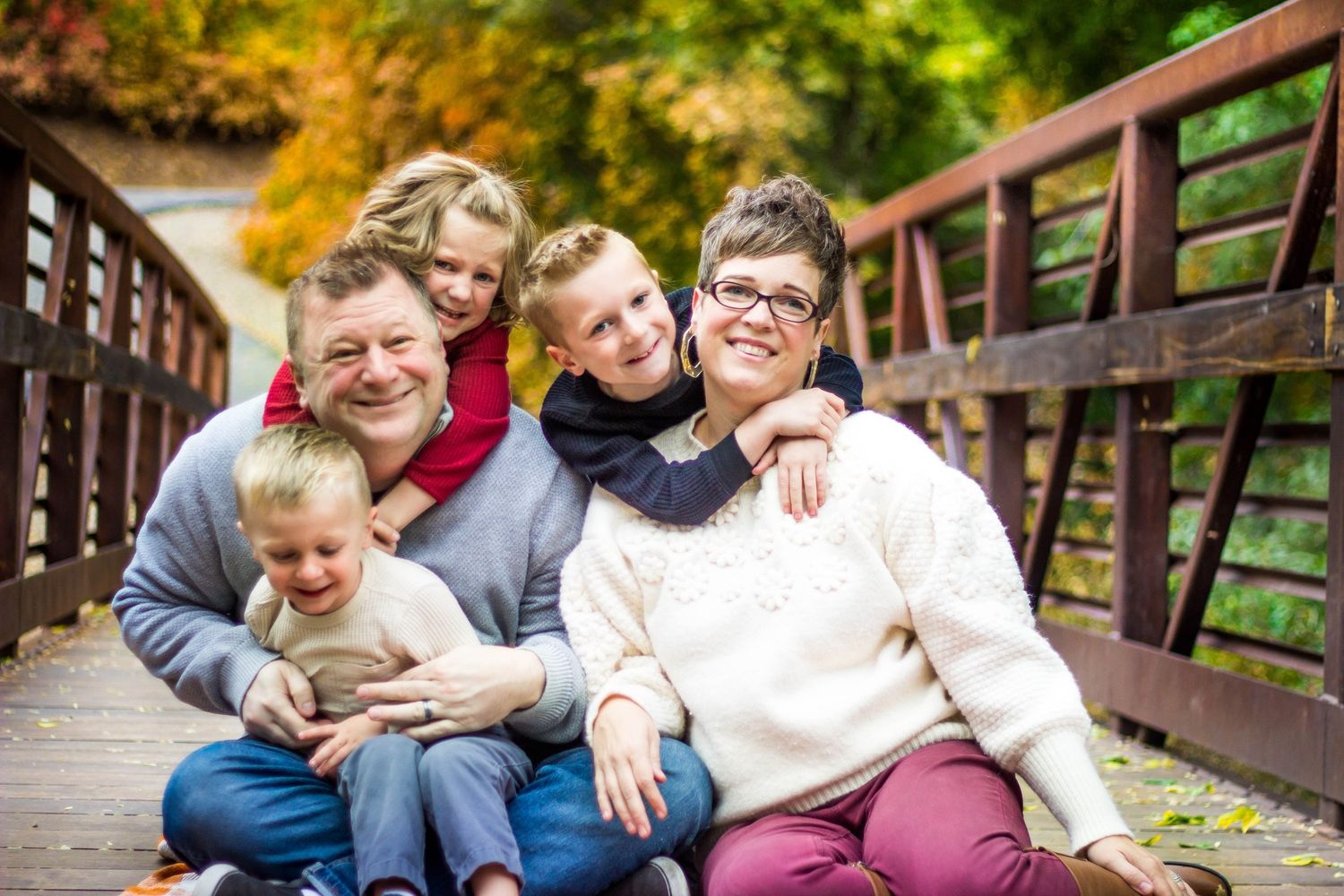Family group laughing together on wooden bridge during fall season.