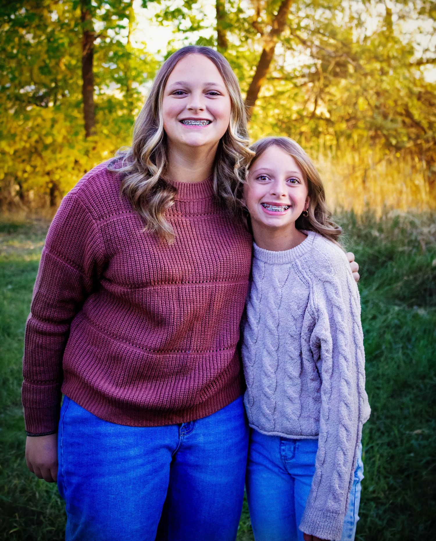Two people in matching sweaters and jeans pose together outdoors during autumn.