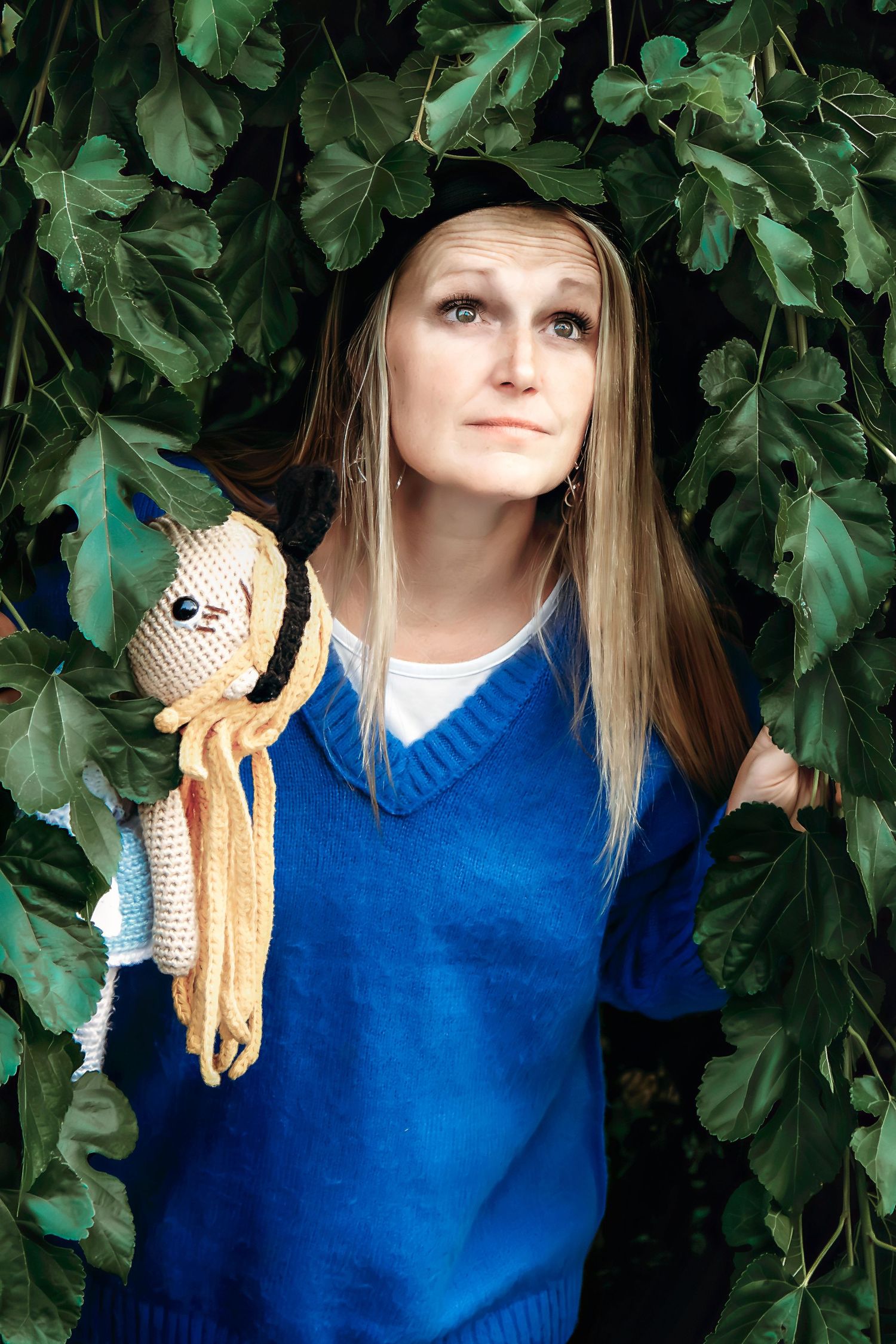 Someone in a blue sweater plays with a handmade crochet doll against a leafy background.