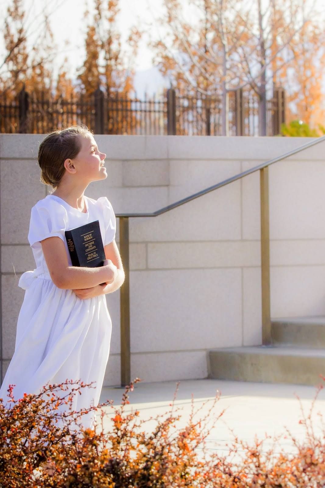 White dress flowing in sunlight against concrete wall with autumn foliage in background.