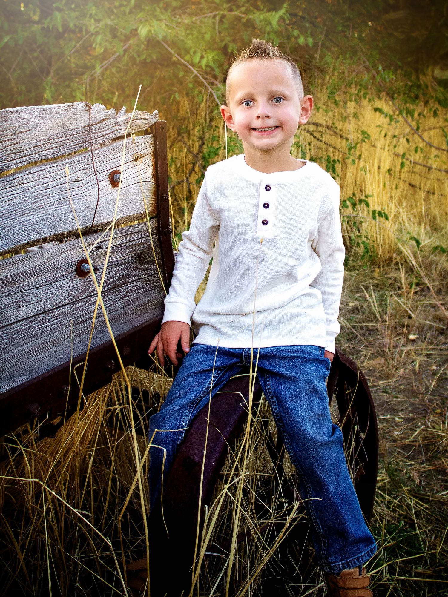 A casual portrait of a child sitting on wooden logs surrounded by tall grass.
