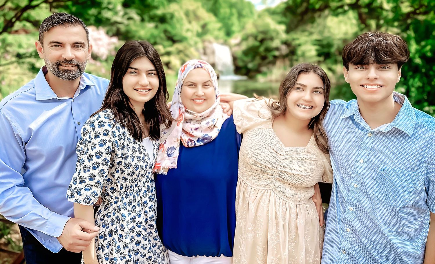 A family portrait of five people wearing coordinated outfits standing together outdoors.