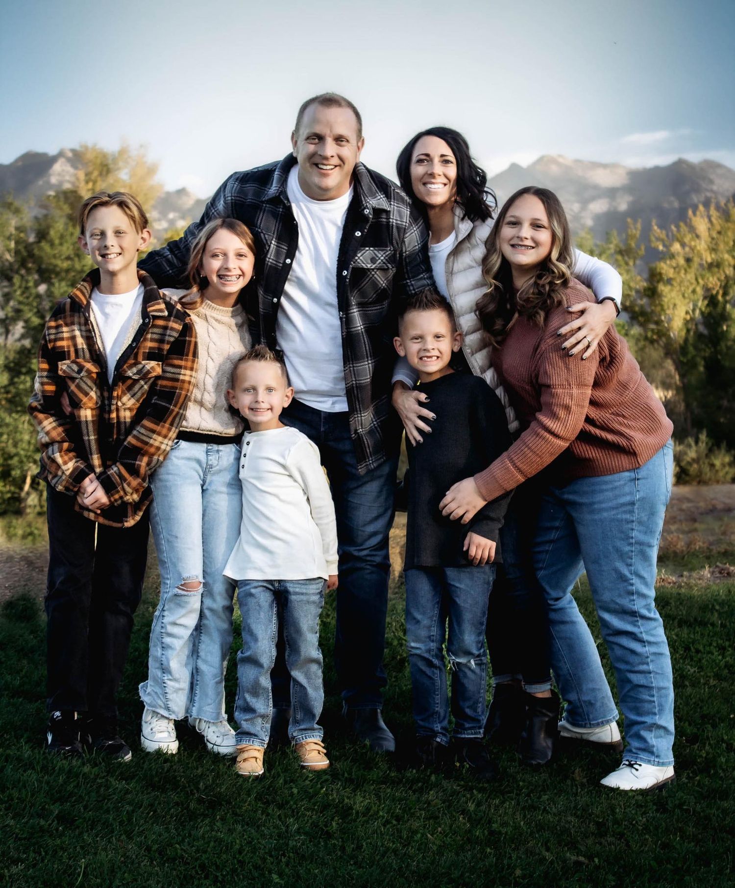 A casual outdoor family photo session with people wearing jeans and arranged in a row against a mountain backdrop.