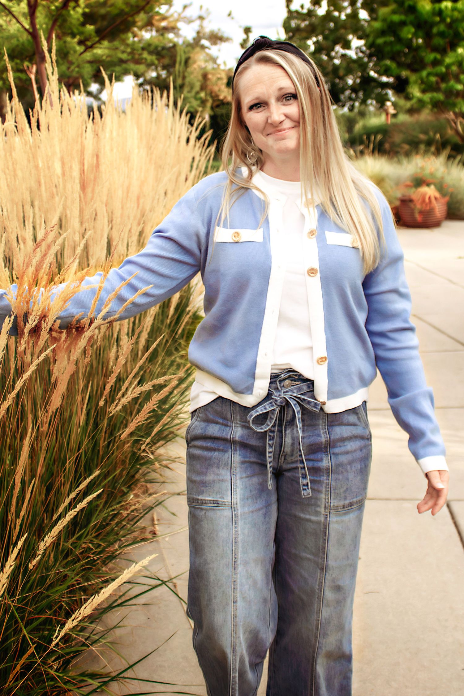 Stylish denim ensemble with light blue jacket shown against ornamental grasses in garden.