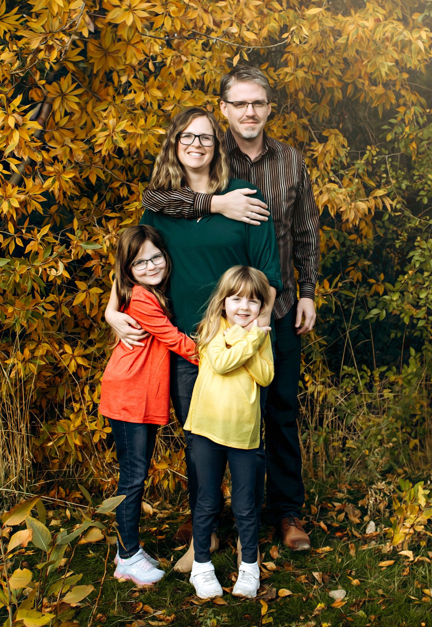 Family portrait in front of yellow autumn leaves and trees.