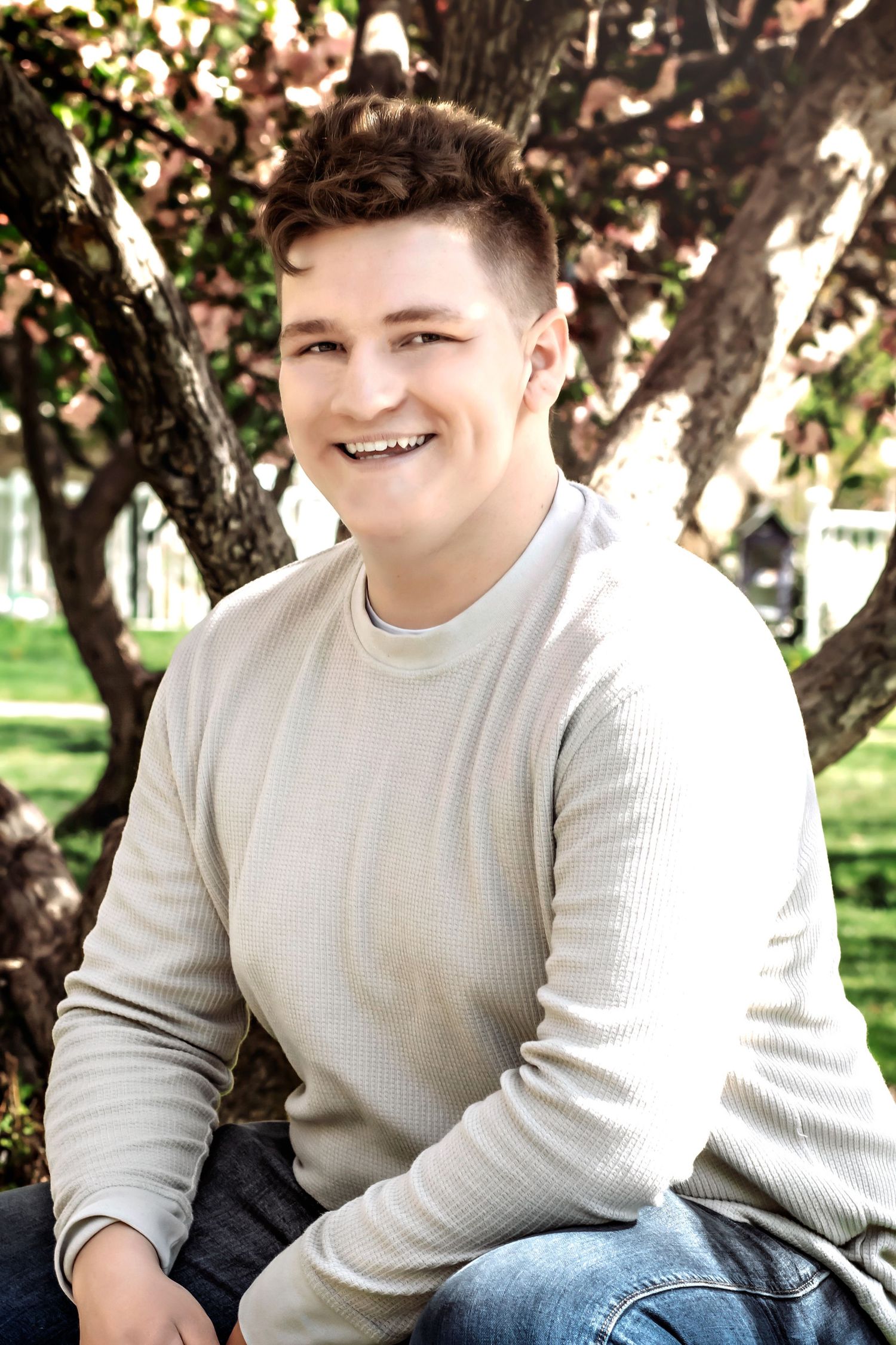 Portrait of someone in a cream sweater sitting outdoors near flowering trees.