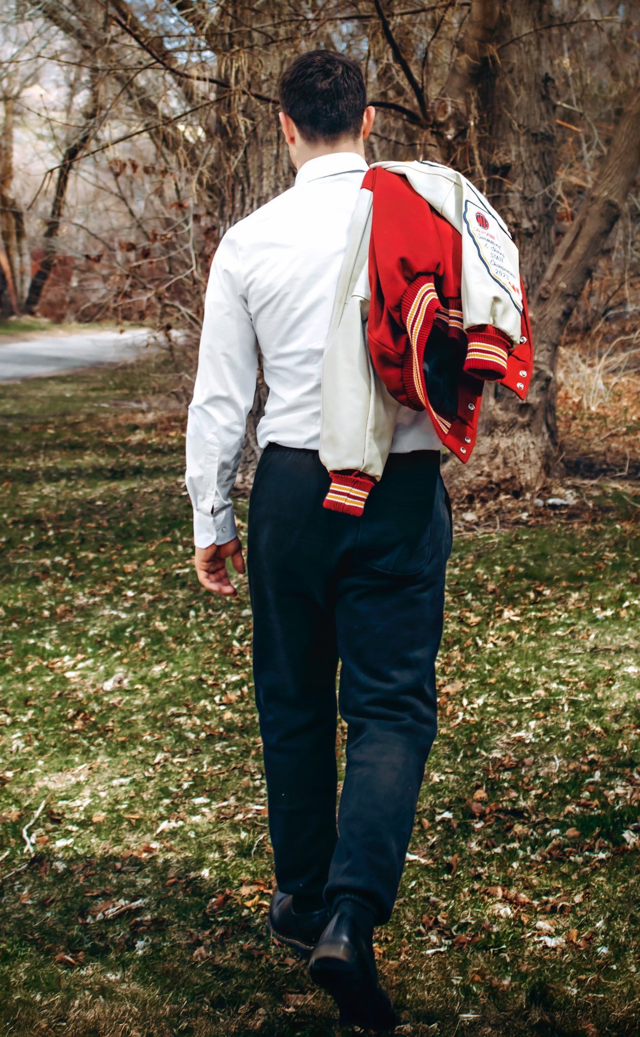 Back view of person carrying red and white varsity jacket while walking on path.