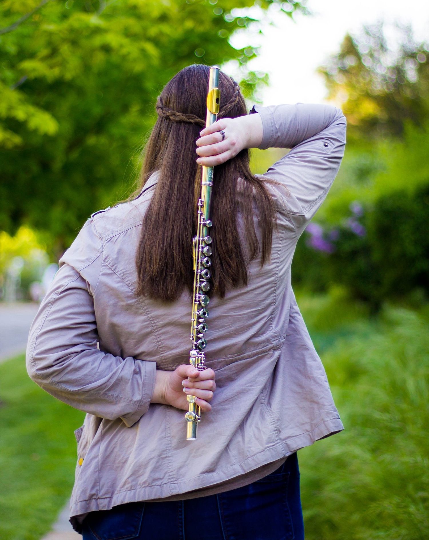 Person in casual clothing holding a musical instrument outdoors with green foliage in background.