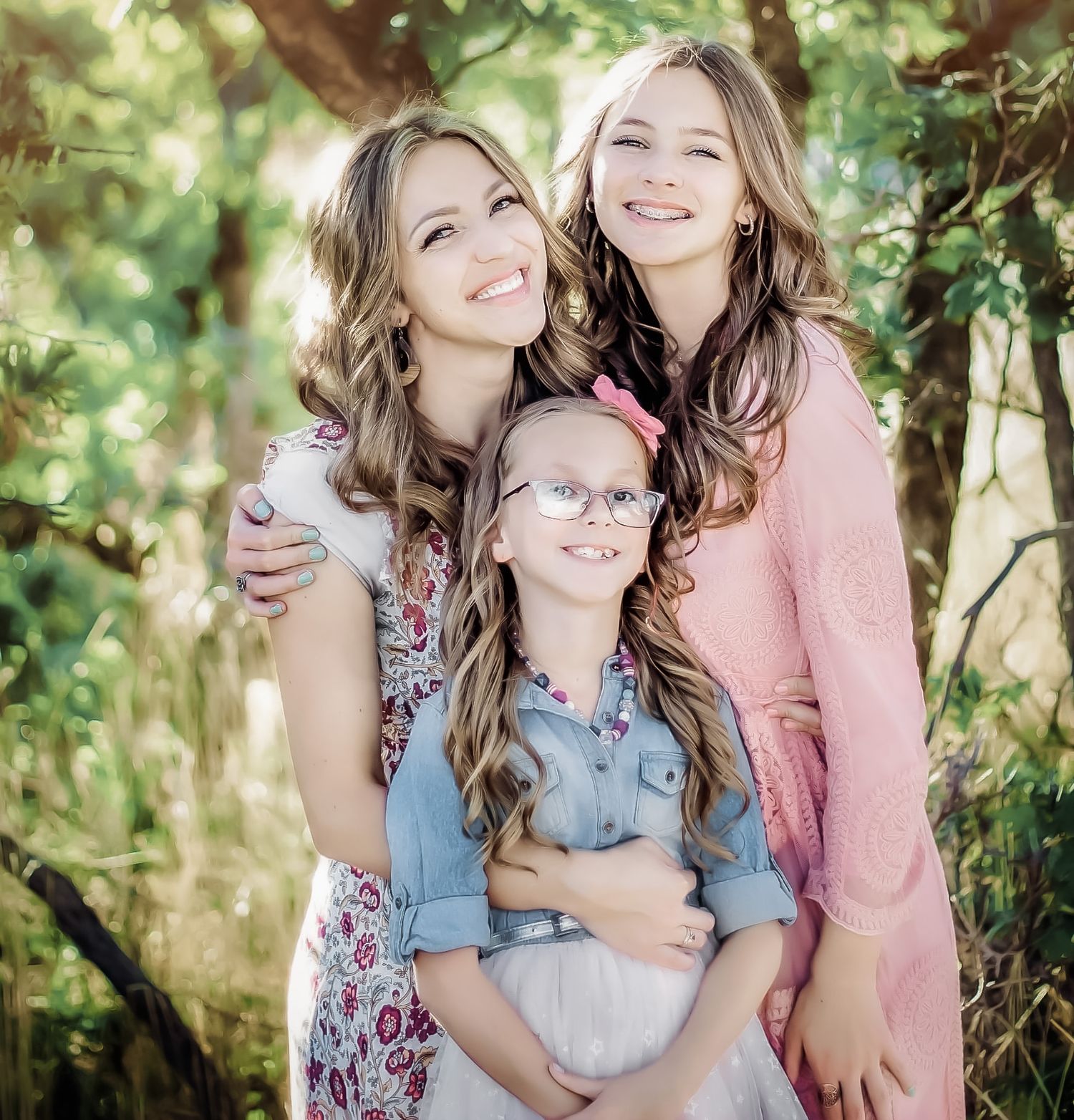Three people embracing and smiling together in a sunny outdoor garden setting.