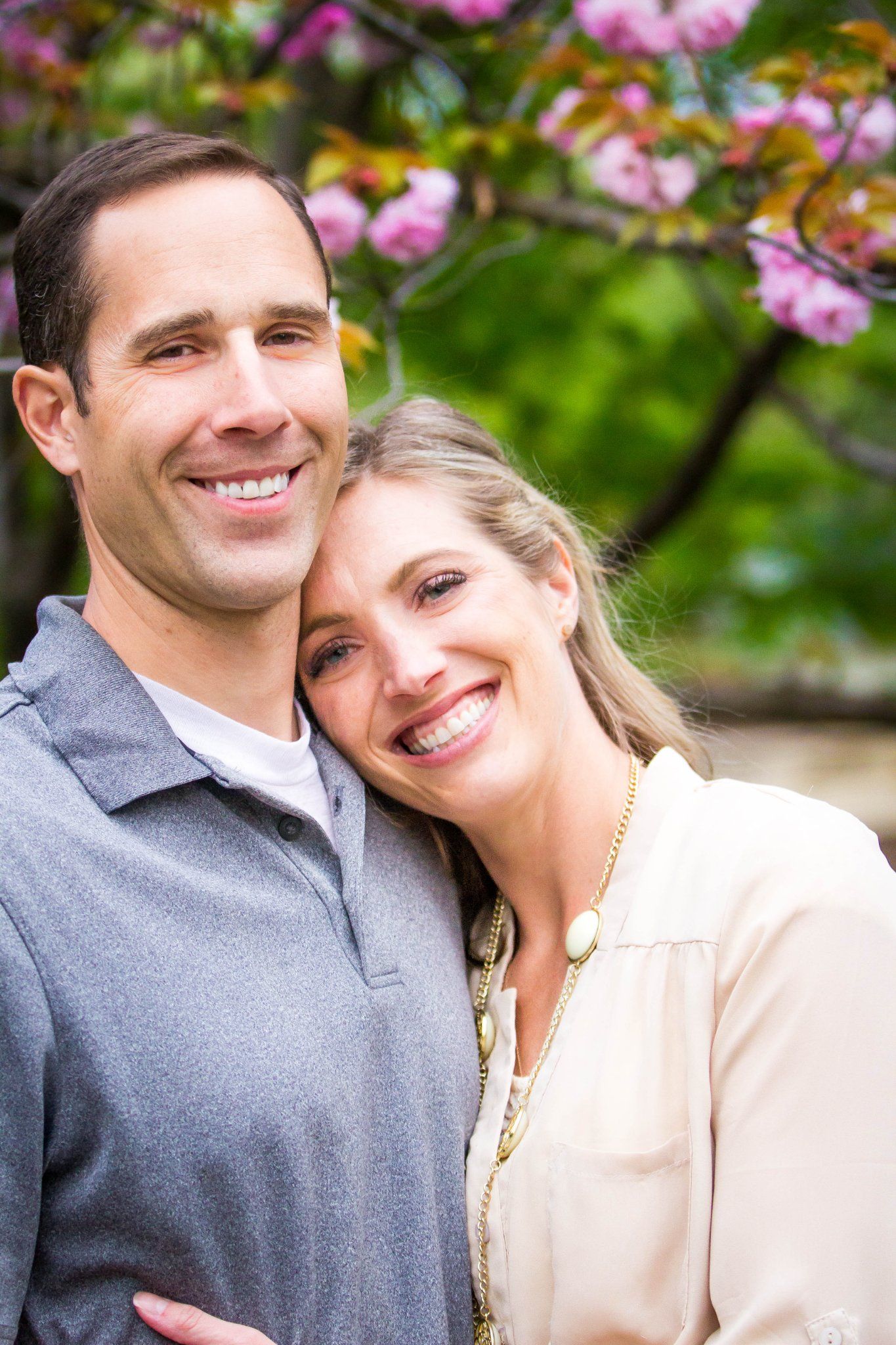 Happy couple embracing outdoors with pink cherry blossoms blooming in the background.