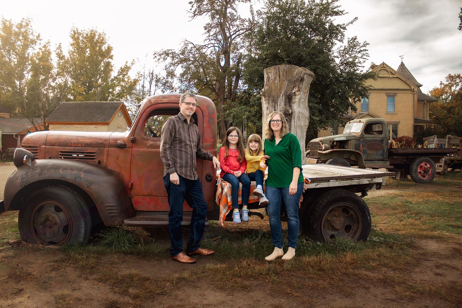 Family portrait session at rustic location with vintage trucks and autumn scenery.