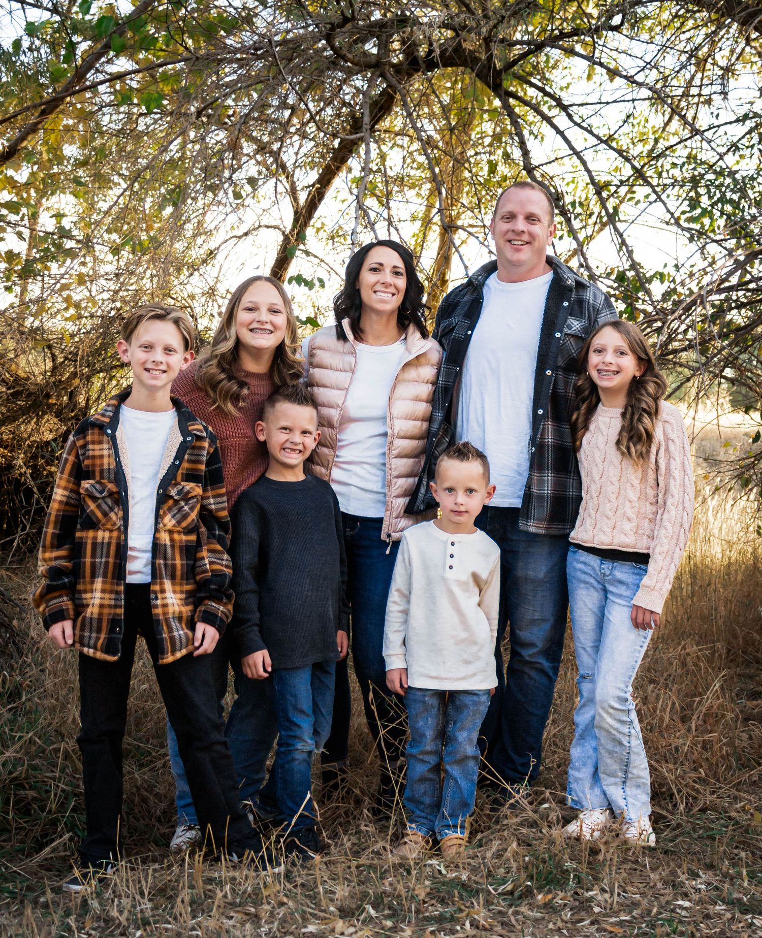Extended family group poses together against natural backdrop of trees and tall grass.