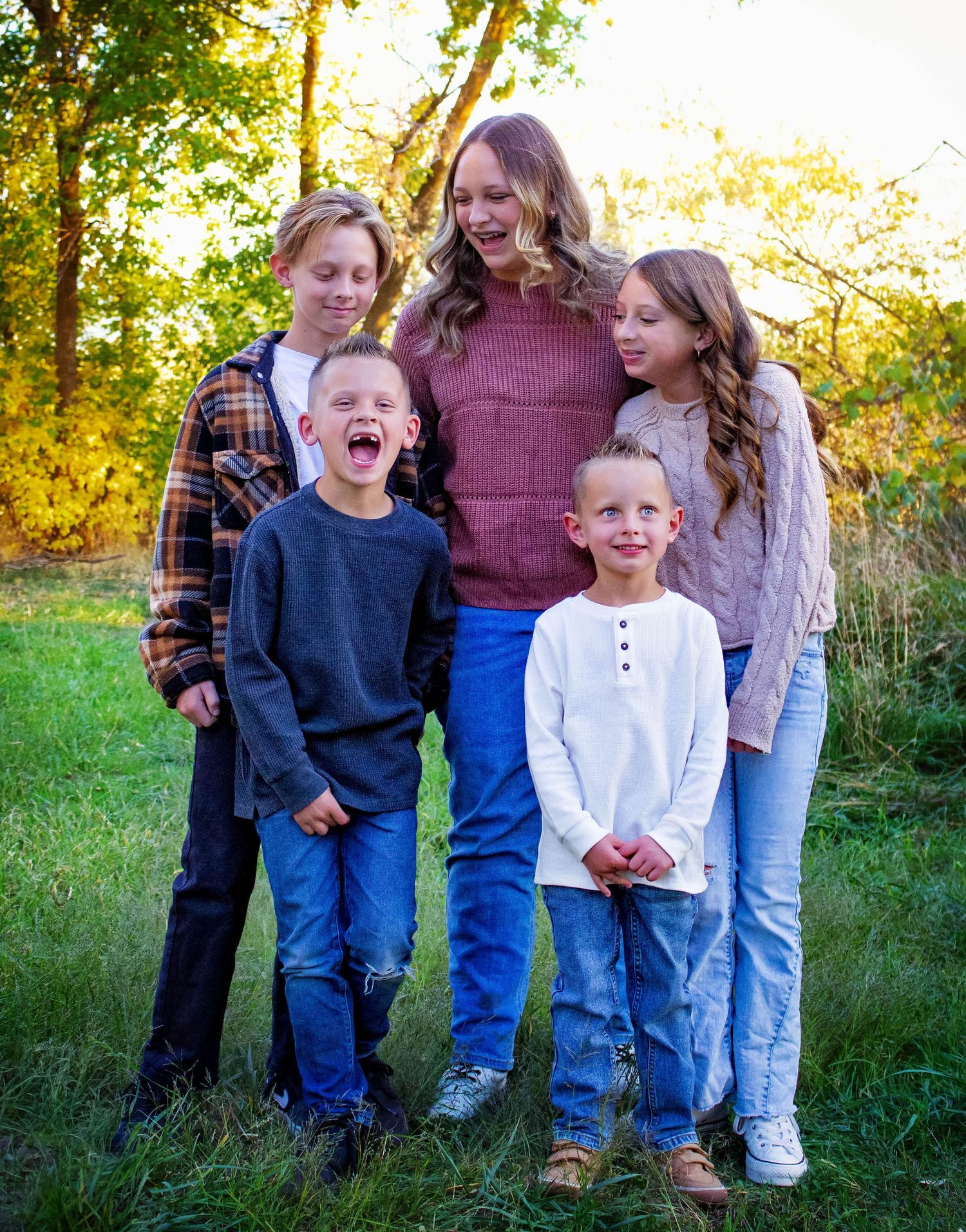 Family portrait outdoors with autumn foliage in background during golden hour.