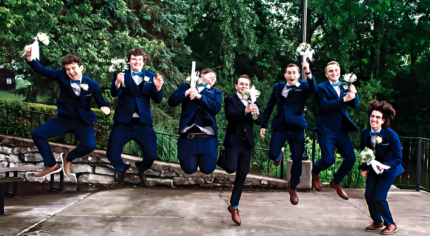 Wedding party in navy suits strikes fun jumping poses outdoors.