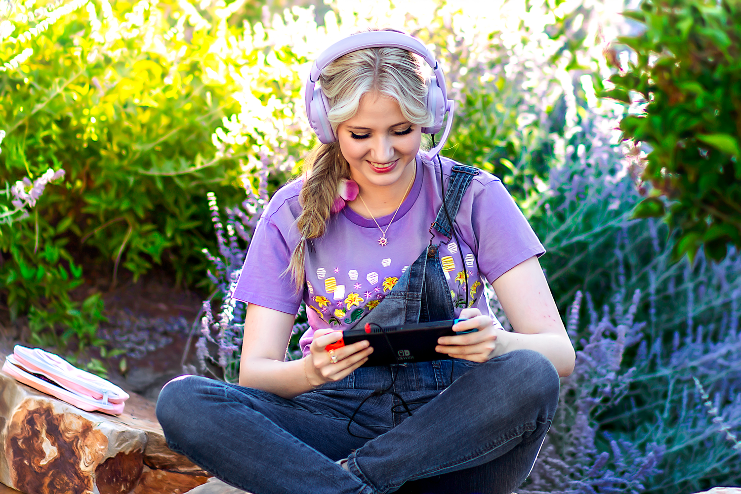 Person in purple shirt and overalls reading while lounging in a garden with flowers.