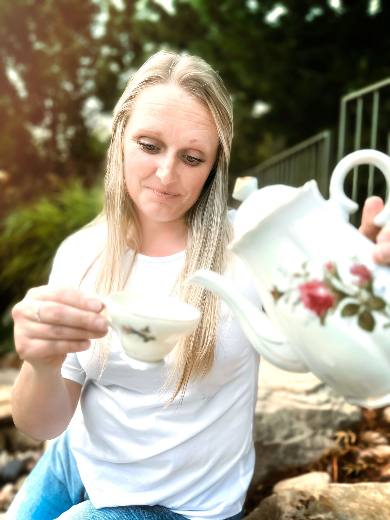 Person pouring tea from decorative teapot in garden setting.