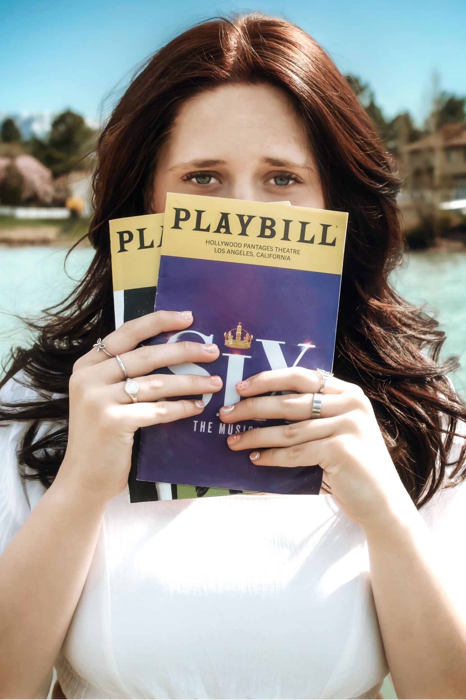 Someone holding Playbill theater programs against a sunny outdoor backdrop.