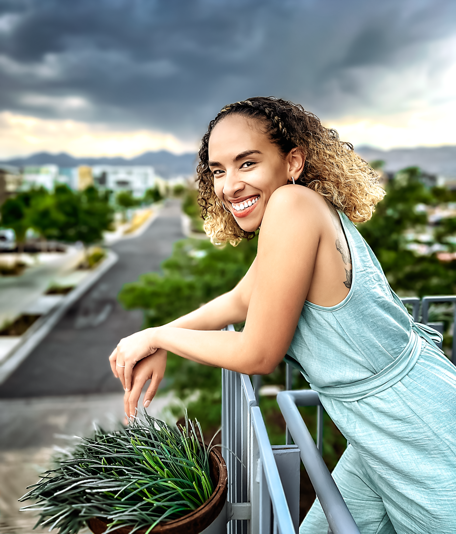 Person in light blue tank top leans on railing against dramatic cloudy sky.