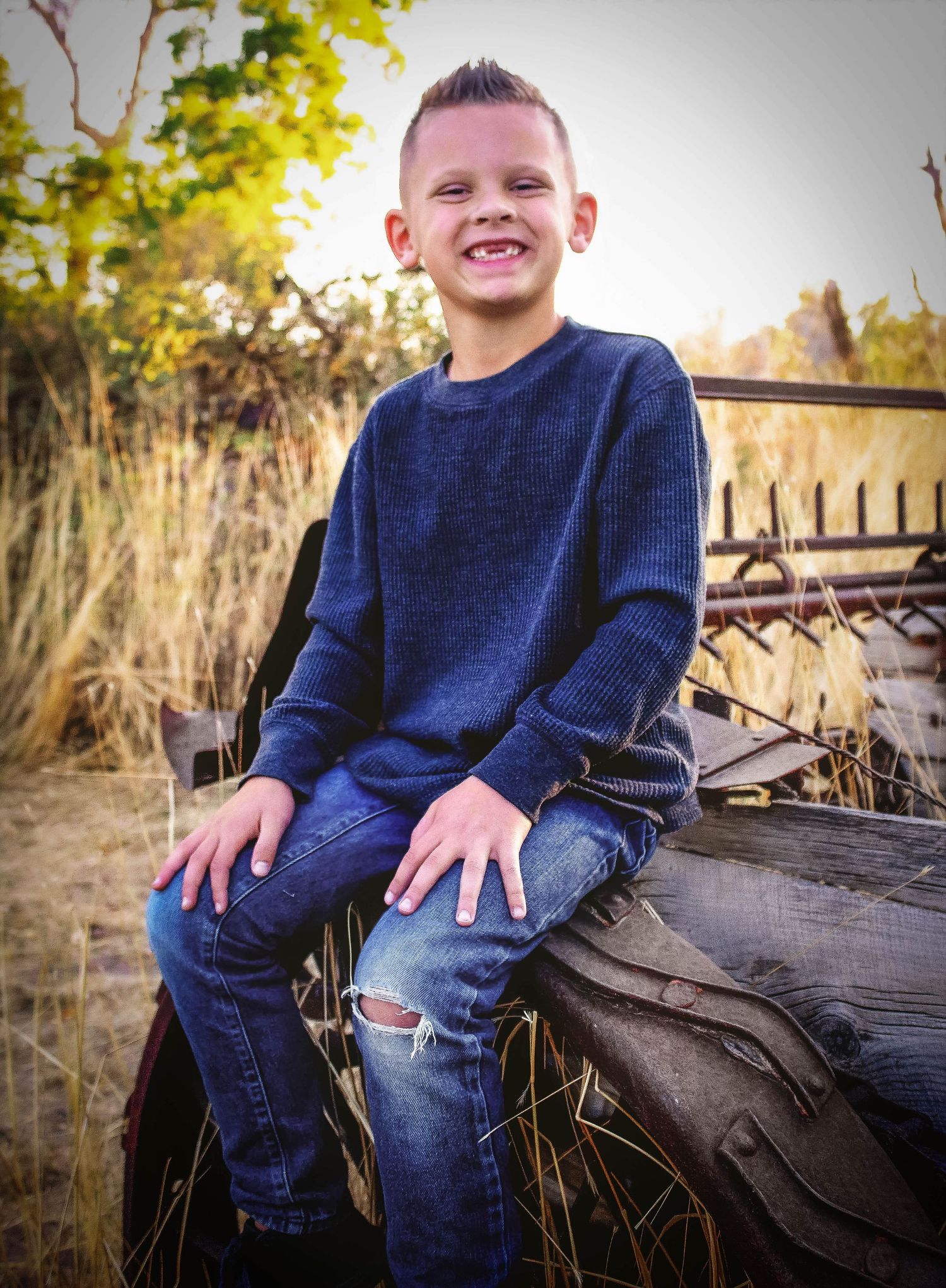 A child in navy sweater sits on rustic wooden logs in an outdoor setting.