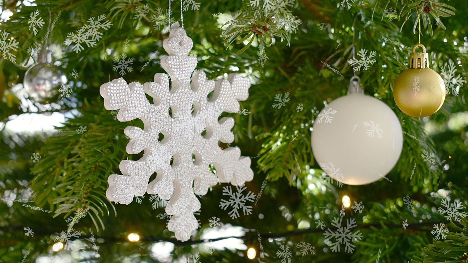 Close-up of white snowflake ornaments and gold baubles hanging on a decorated Christmas tree with twinkling lights.