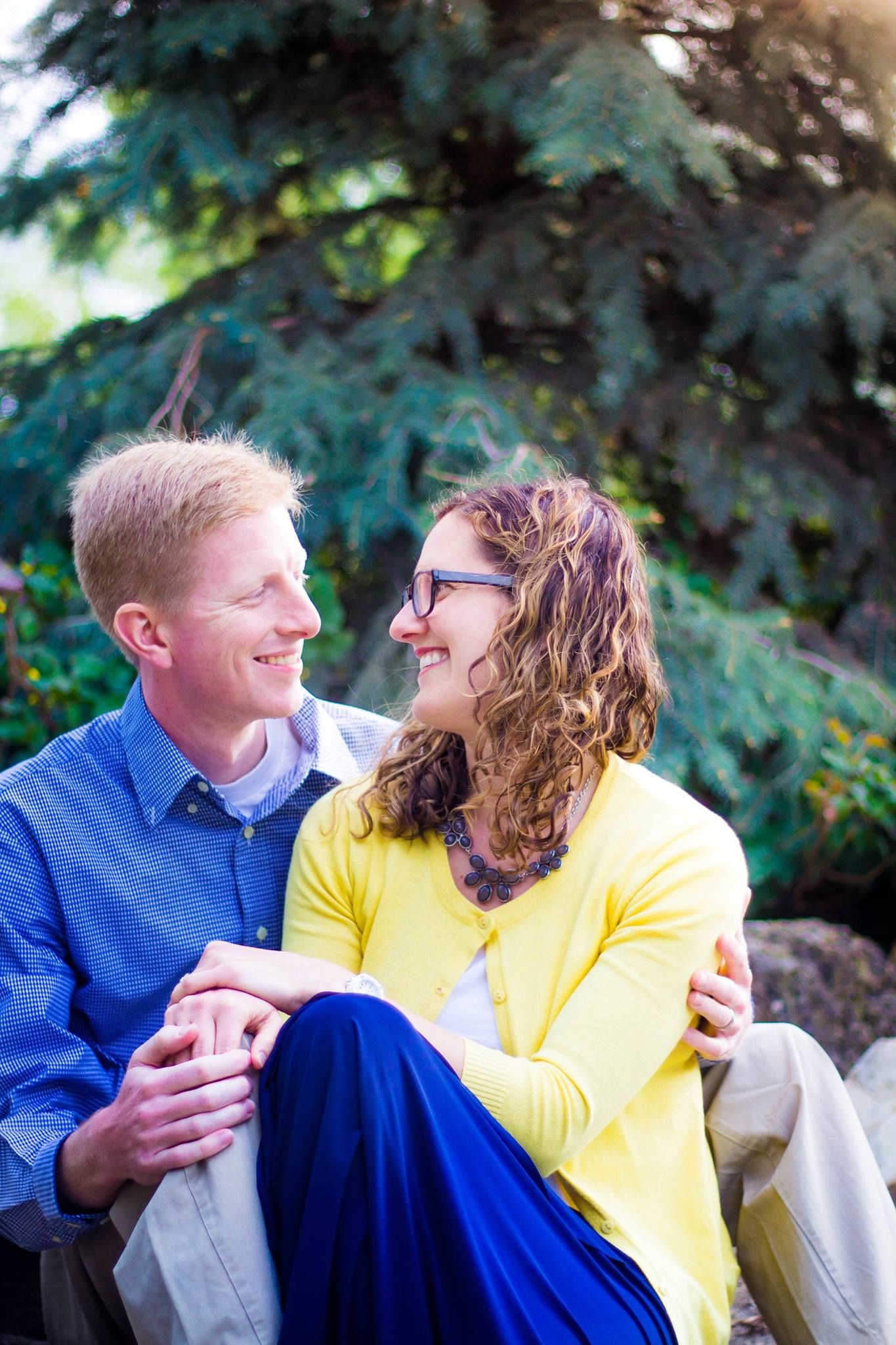 Happy couple in casual attire sharing genuine laughter during outdoor portrait session.