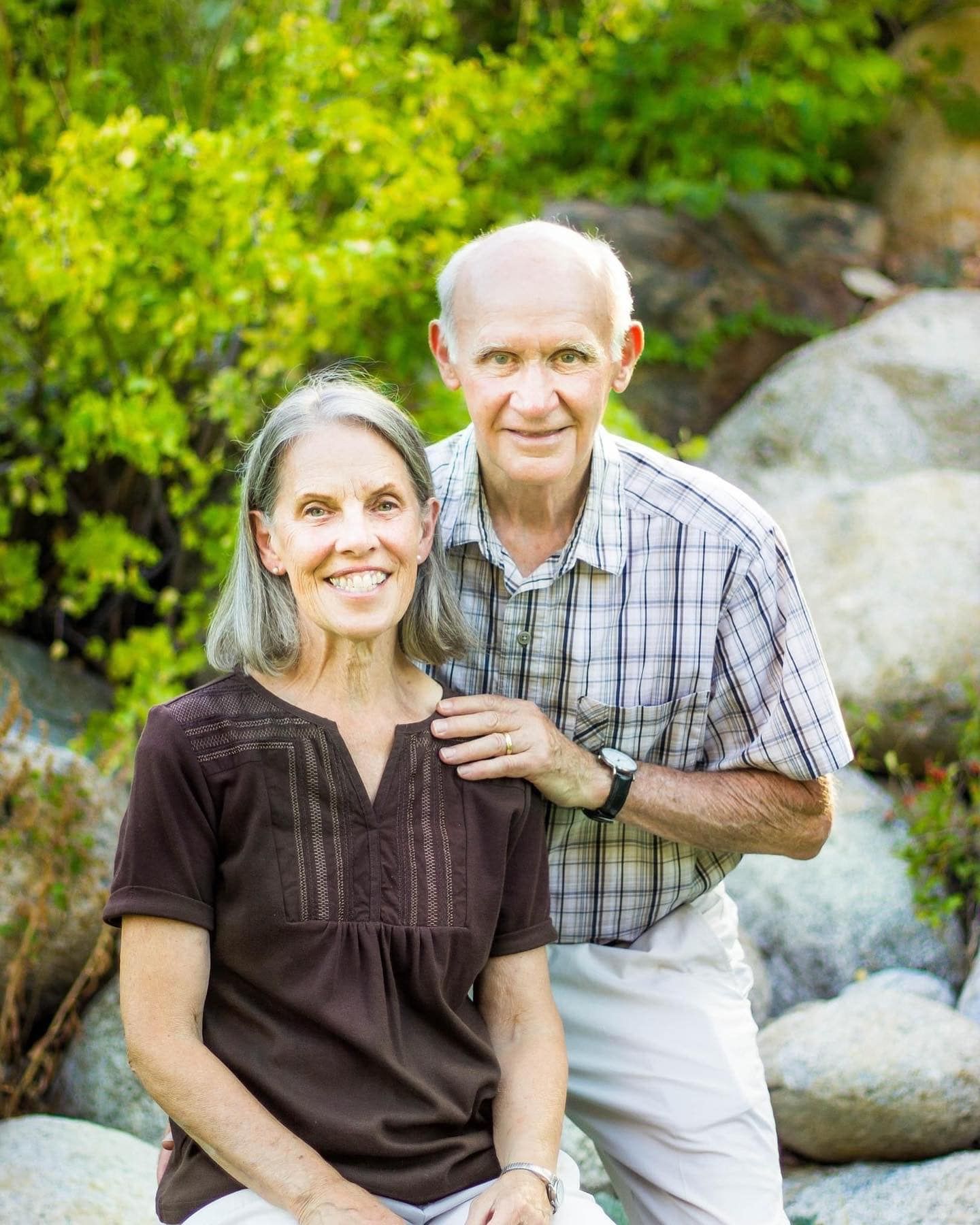 Couple sitting together on rocky outcrop with lush green foliage behind them.