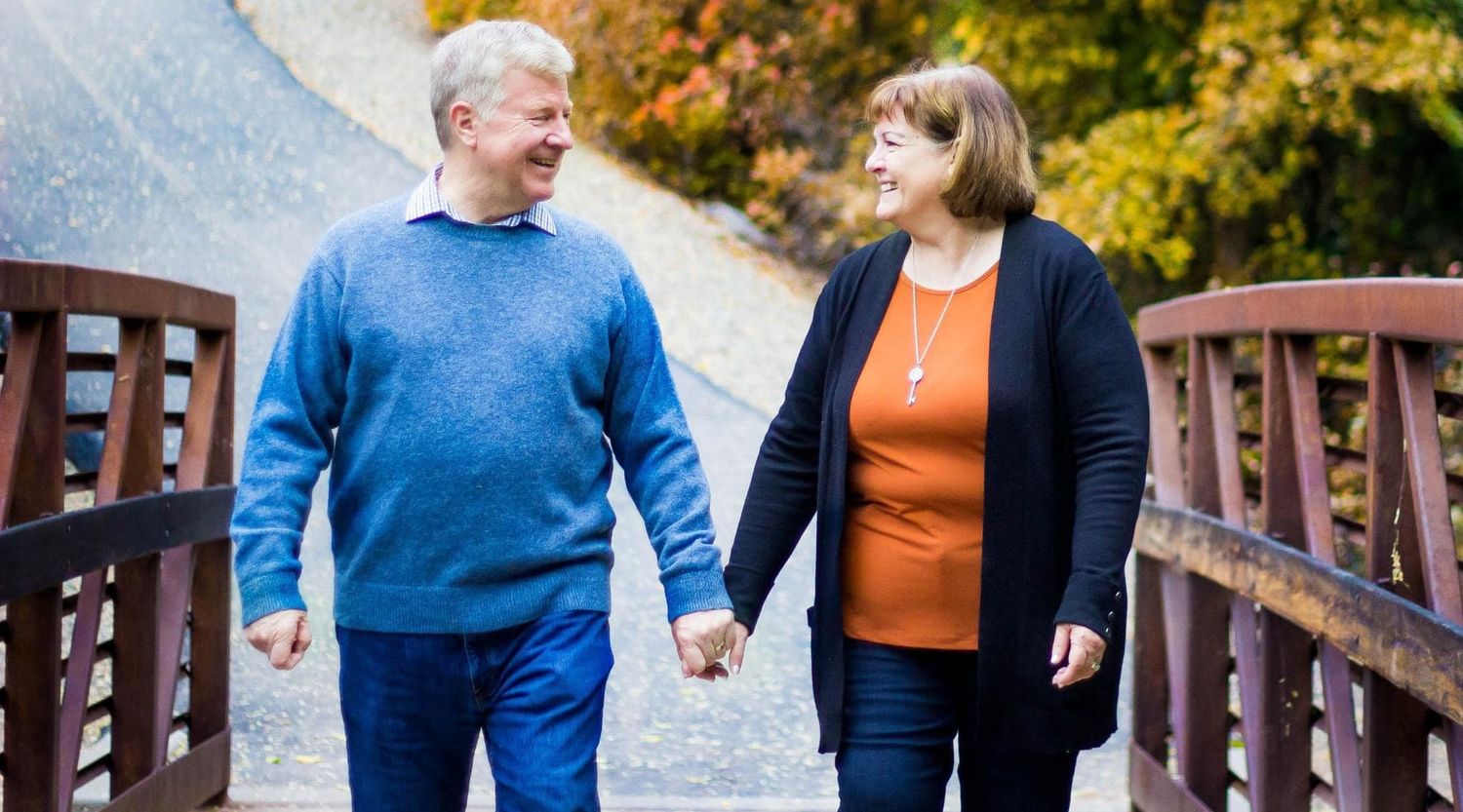 Couple holding hands while walking on wooden bridge during autumn season.