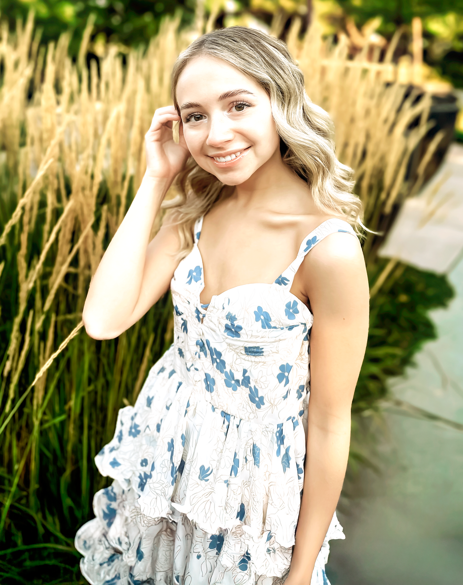 Portrait session by tall grass wearing a white and blue patterned summer dress.