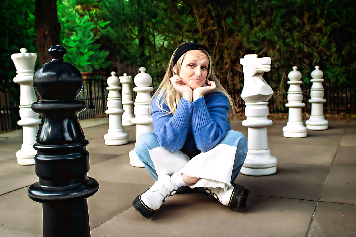 Person in blue sitting among large outdoor chess pieces.