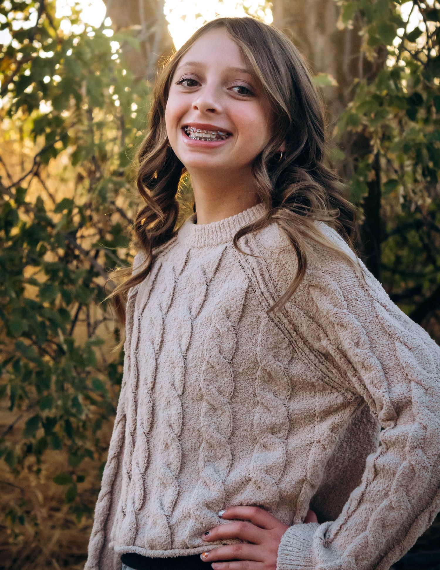 Woman wearing a cozy beige cable knit sweater poses outdoors in autumn setting.