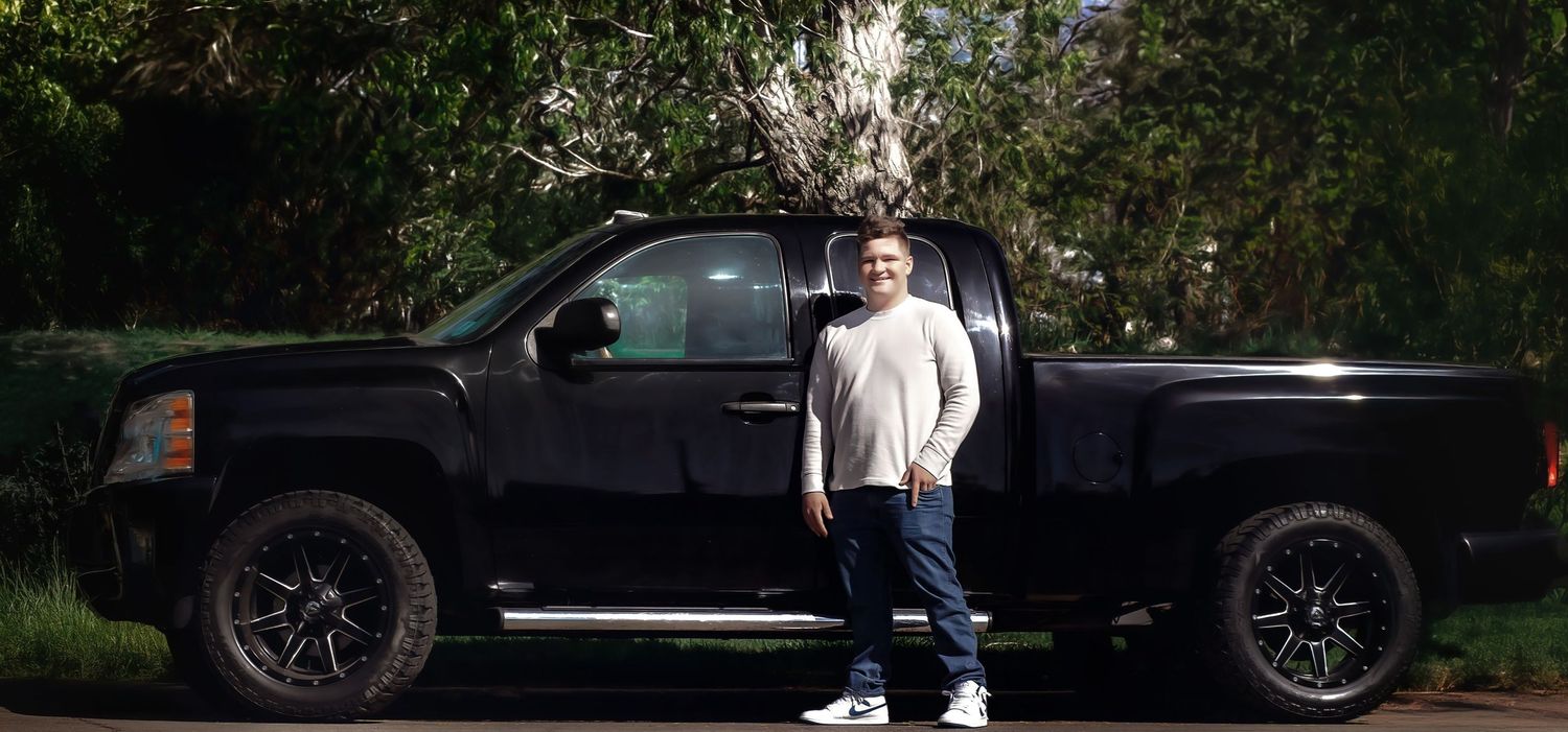 Black pickup truck with custom wheels parked under trees.
