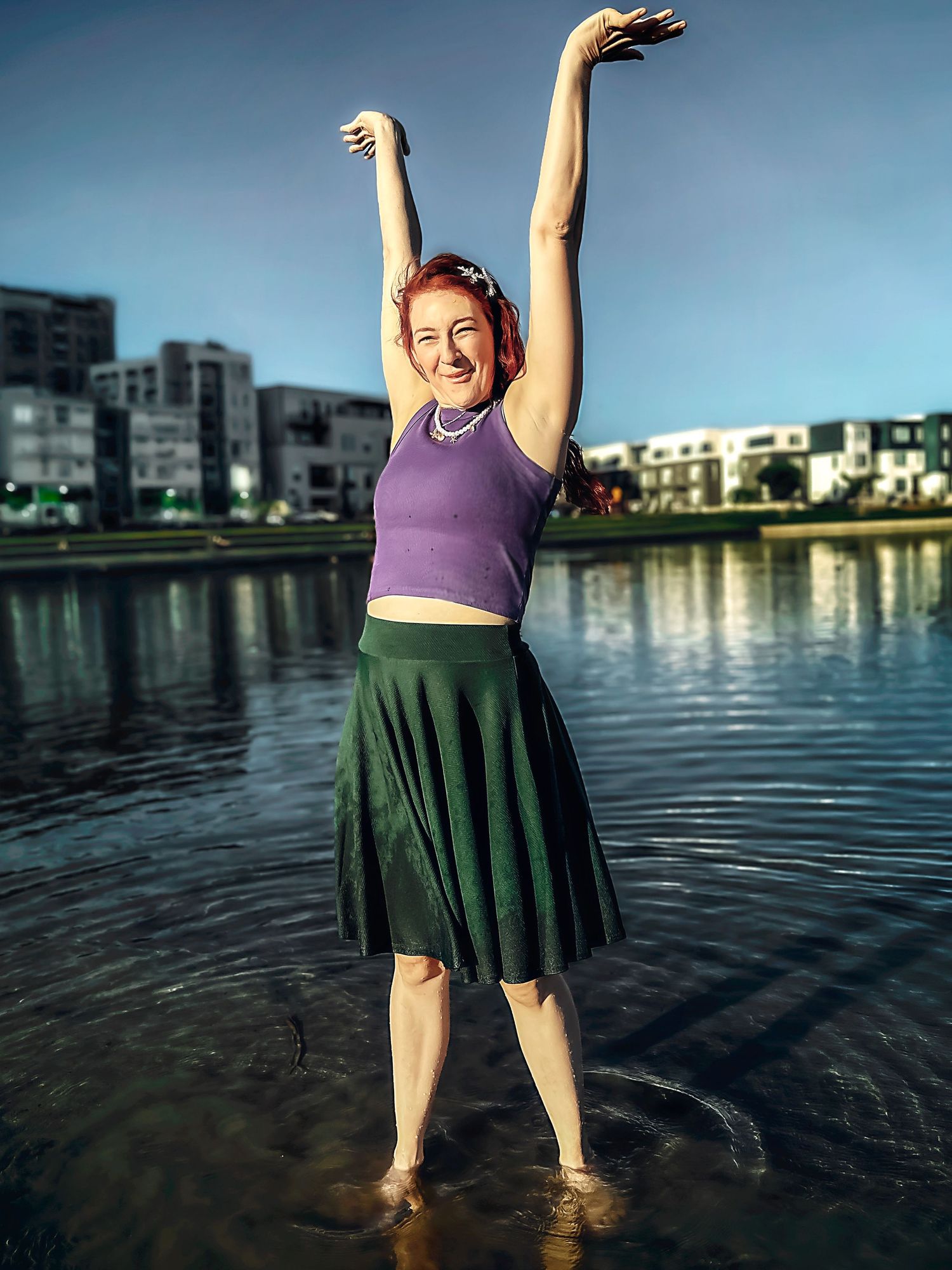 A person in a purple top and dark skirt splashing in the water at sunset.