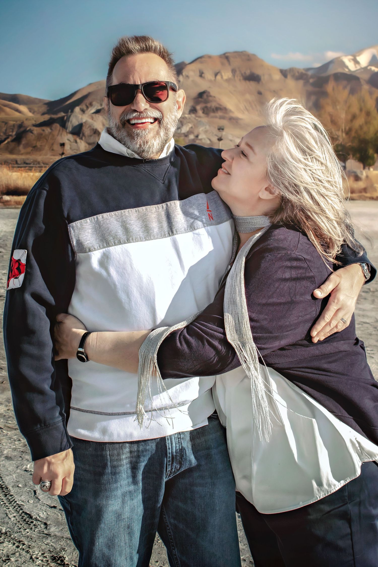 Couple laughs together during casual outdoor photoshoot with desert mountains in background.