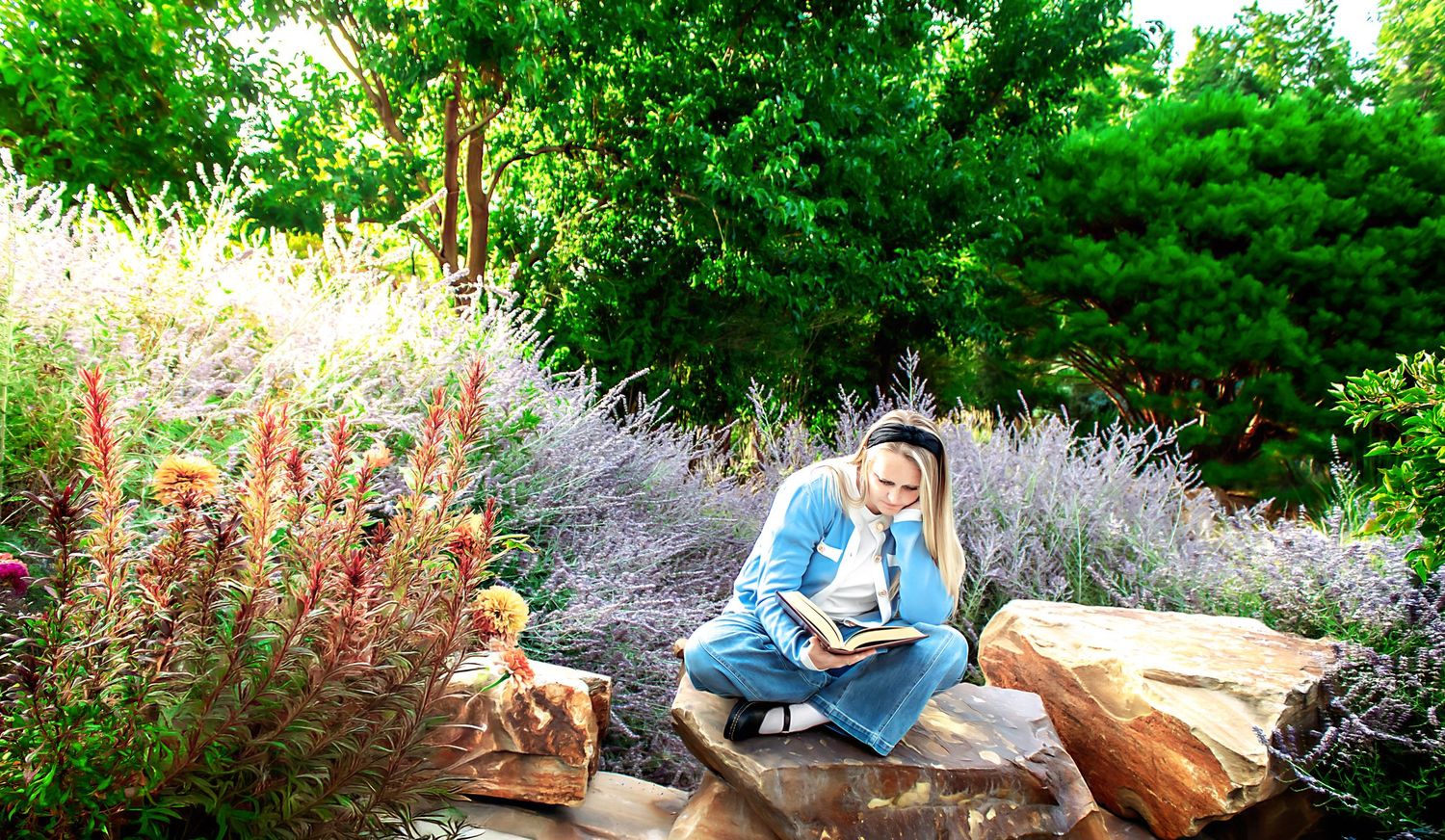 Figure in denim and blue jacket walks along garden path with flowering plants and greenery.