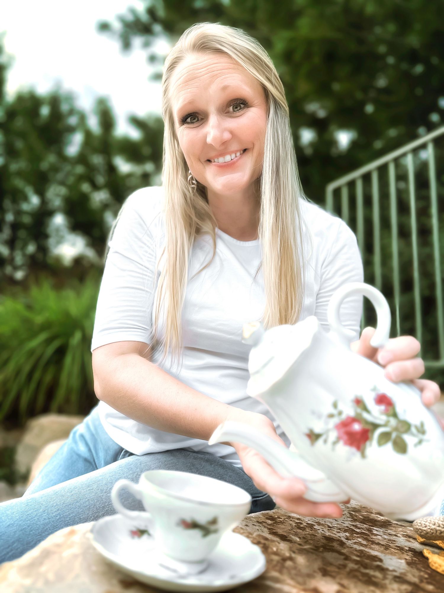 Woman in white shirt enjoying tea from vintage floral teacup set outdoors.