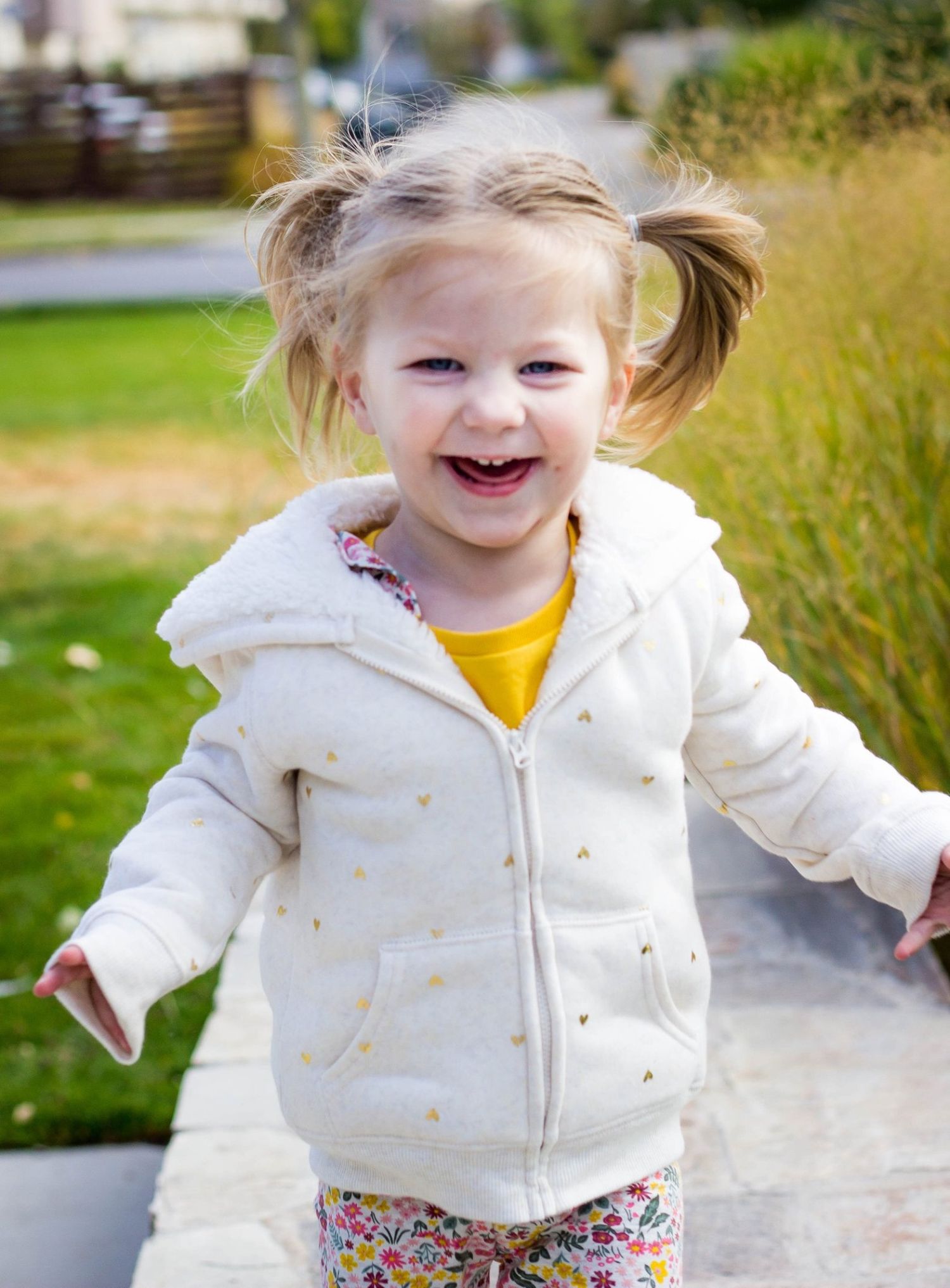 Young child in white jacket jumps and plays outdoors with pure joy.