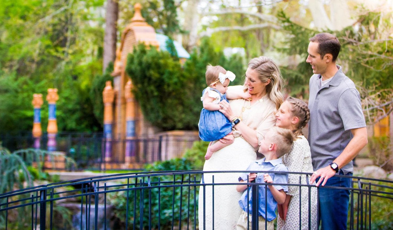 A family enjoying a moment together at a theme park railing with decorative buildings in the background.