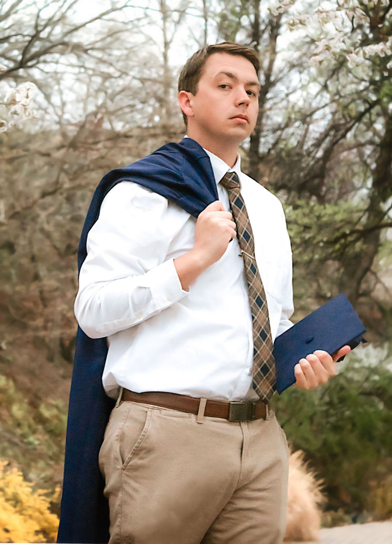 Person adjusting tie while wearing business attire outdoors in autumn setting.