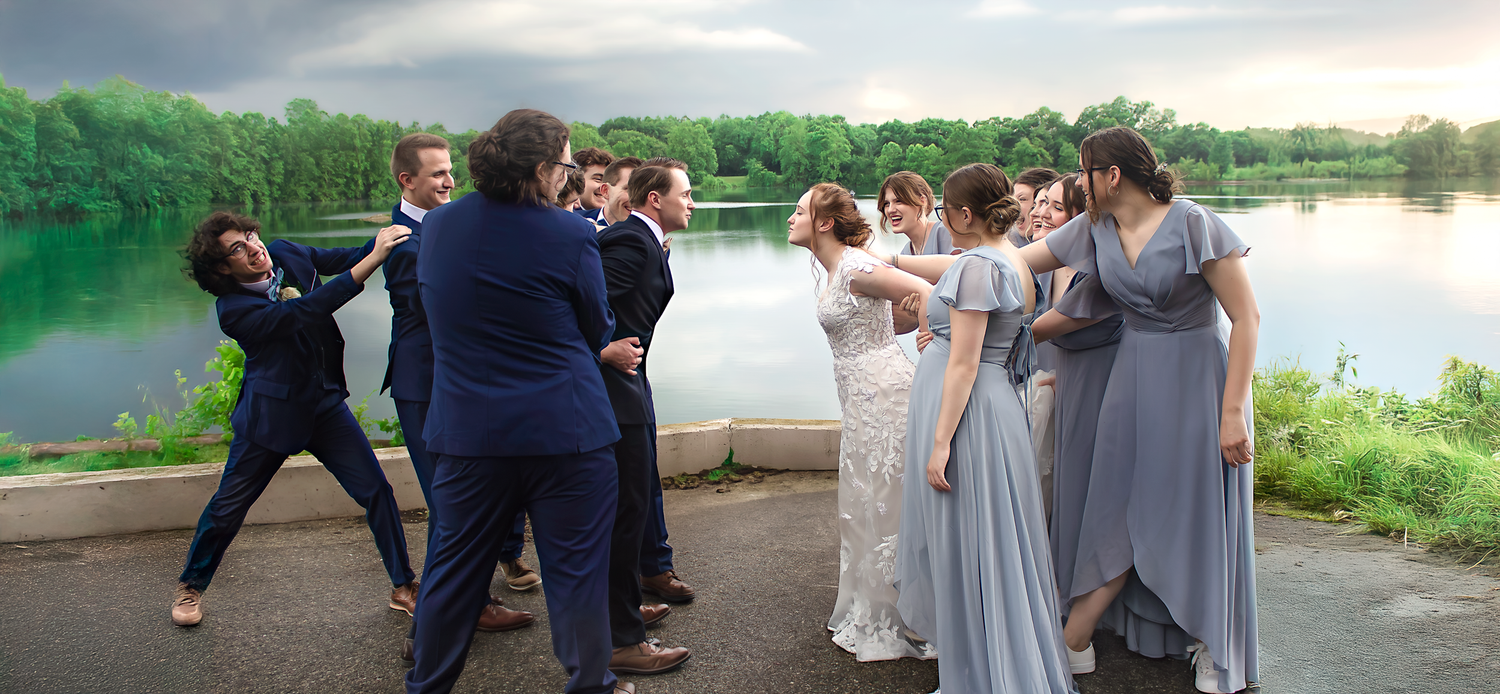 Wedding party gathered outdoors near a lake at sunset.