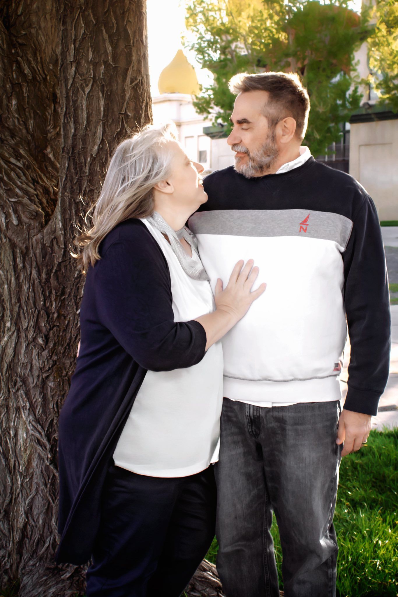 Couple in navy and white clothing share tender moments against a tree backdrop.