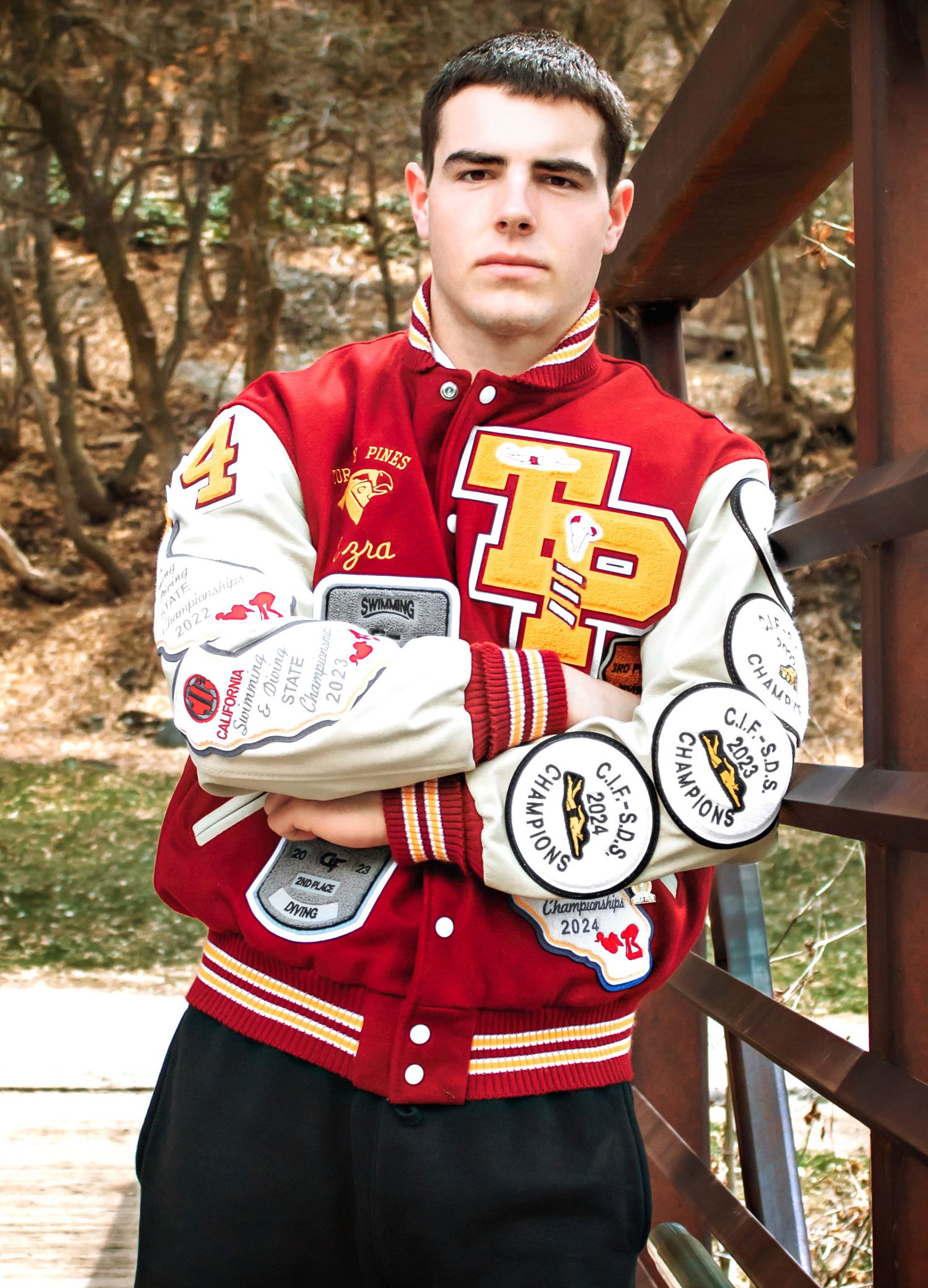 Red and white varsity letterman jacket with patches and emblems shown in outdoor setting.